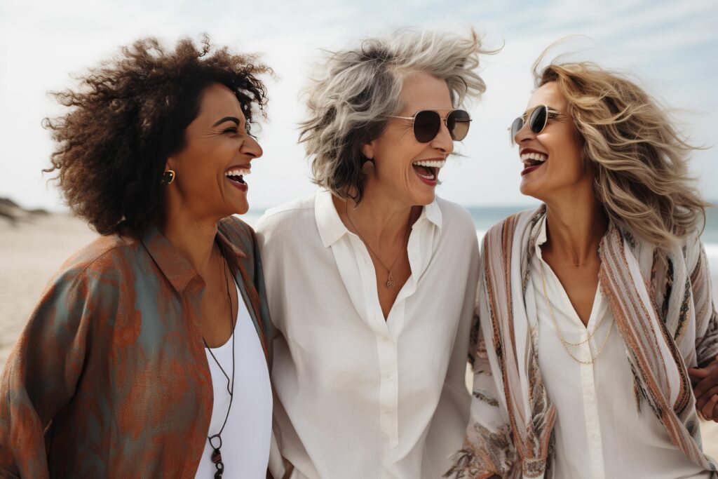 Drei Frauen unterschiedlichen Alters lachen miteinander am Strand.