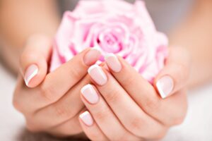 Damenhände mit French-Nails halten eine rosafarbene Rose.
