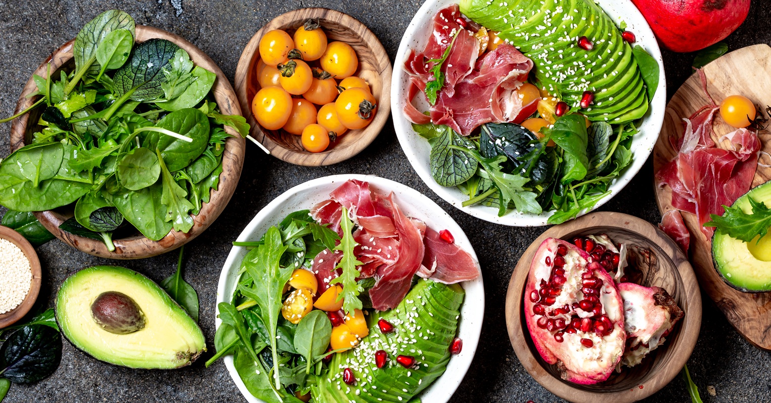 Bowls mit Spinat, gelben Tomaten, Avocado, Rucola, Schinken und Granatapfel.