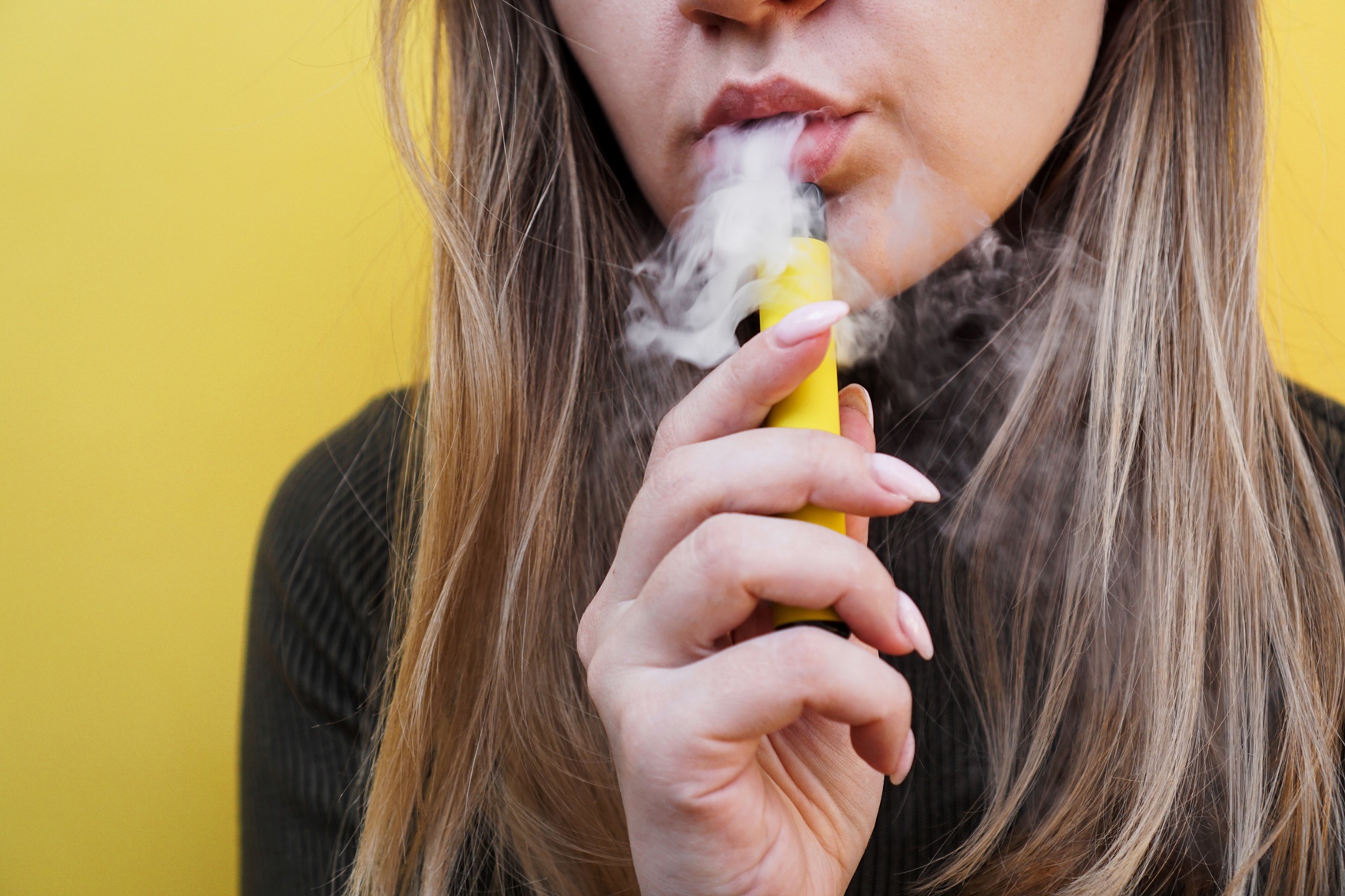 Junge Frau mit Vaporizer in der Hand atmet Dampf aus.