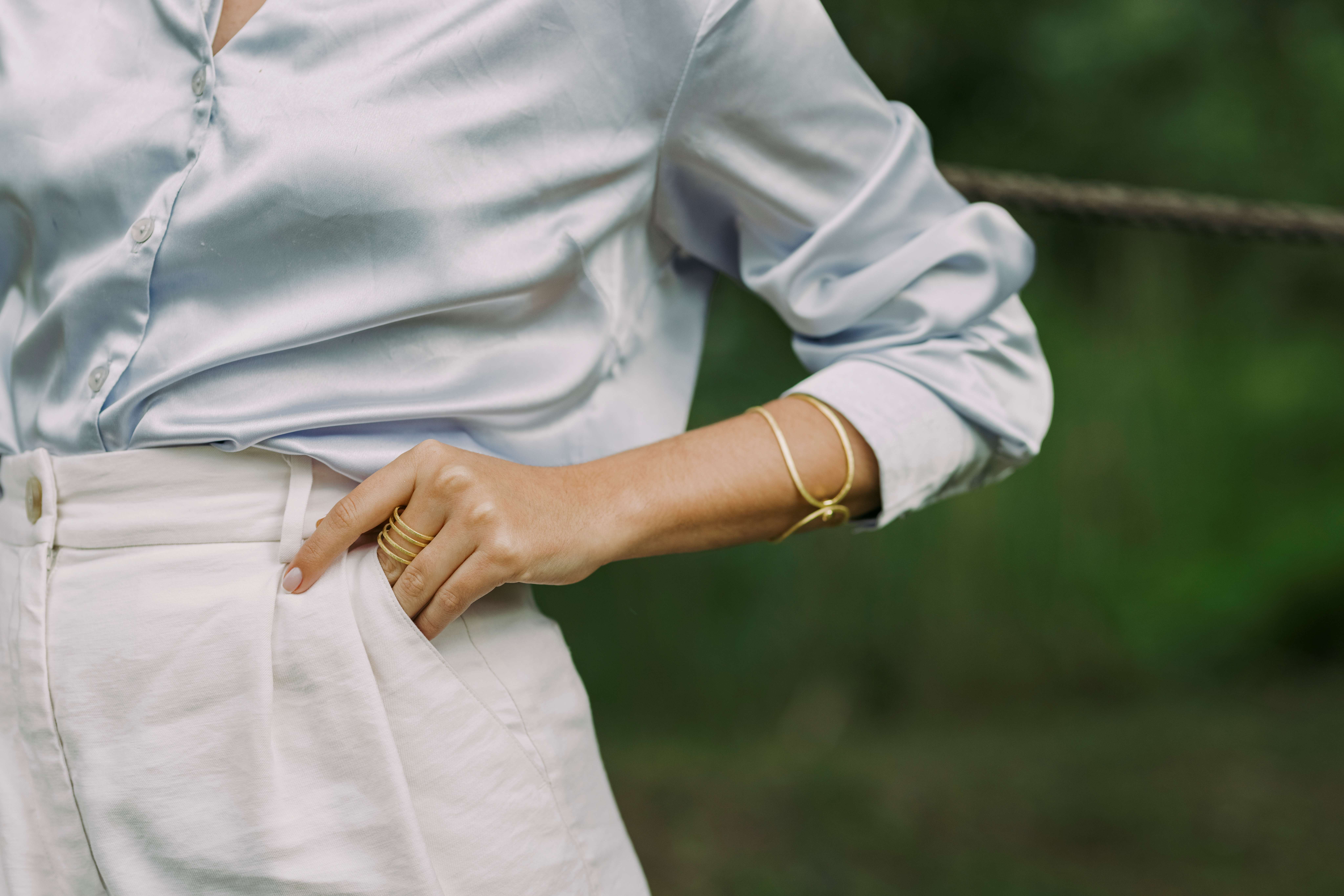 Nahaufnahme des Arms einer Frau mit Goldarmband und goldenem Ring am Finger.