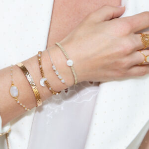 Hand und Unterarm mit einigen Ringen und Armändern in Gold und mit Edelsteinen zu sehen.