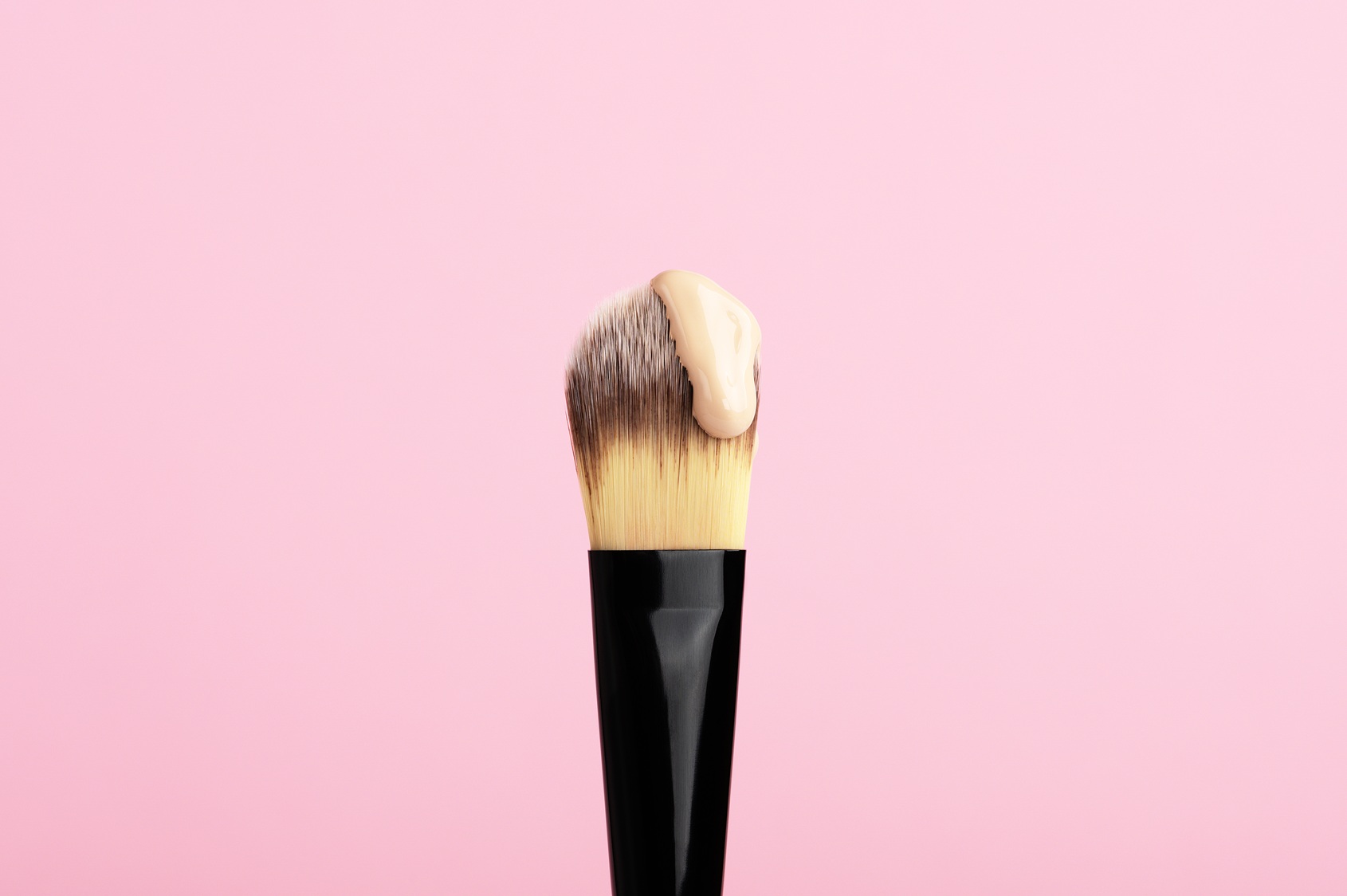 Pinsel mit Foundation vor einem rosa Hintergrund.