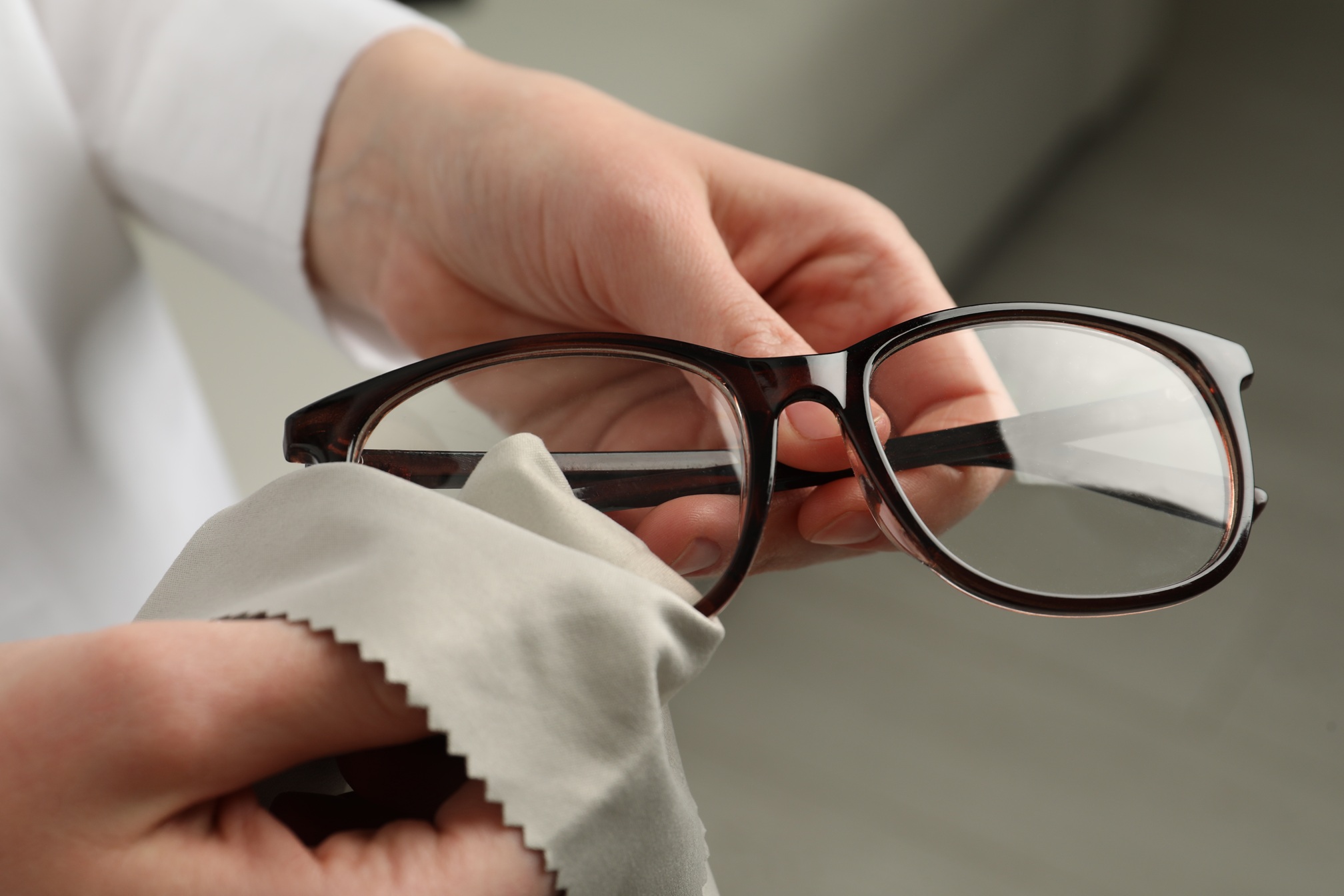 Die Gläser einer Brille werden mit einem Mikrofaserputztuch gesäubert.