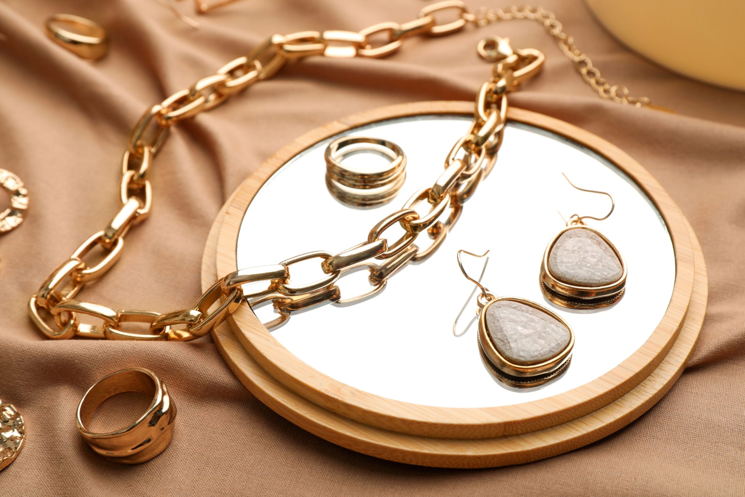 Eine Kette, Ringe und Ohrringe liegen auf einem Spiegel und einem braunen Tuch.