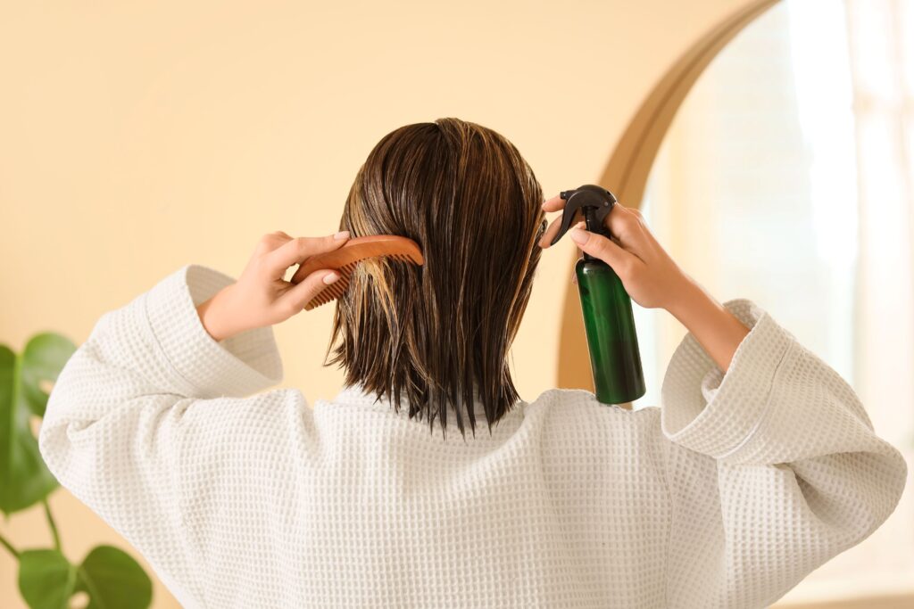 Ein Frau kämmt sich mit einem Kamm die nassen Haare und hält ein Pflegespray in der Hand.