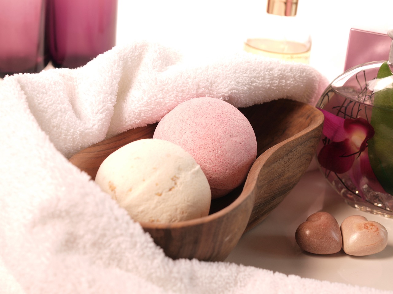 Zwei Badekugeln liegen in einer Holzschale vor einem farblich passenden Handtuch.