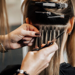 Eine Friseurin bring bei einer Frau Extensions an.