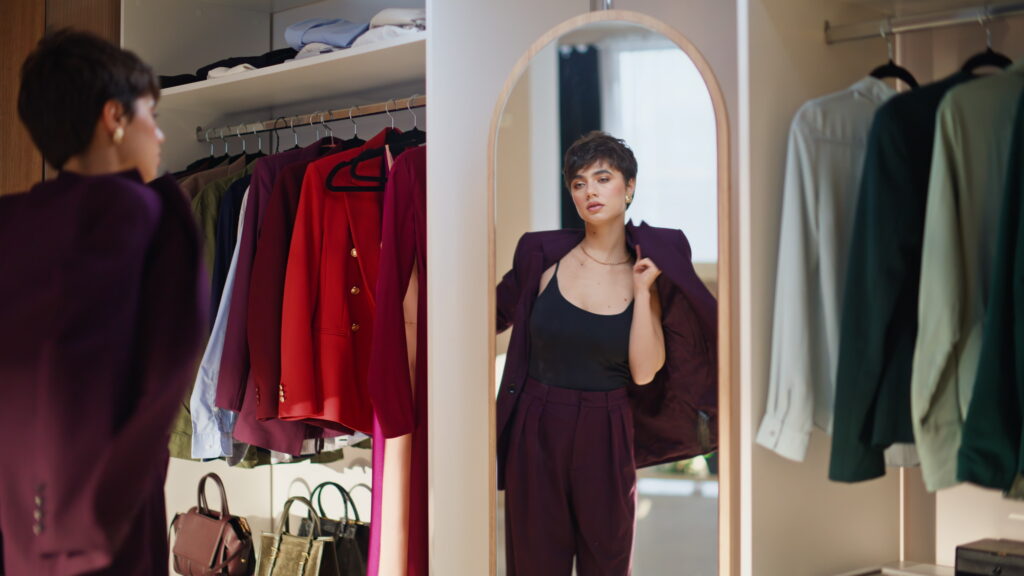 Eine Frau steht in einem Ankleideraum und zieht einen dunklen Anzug an.