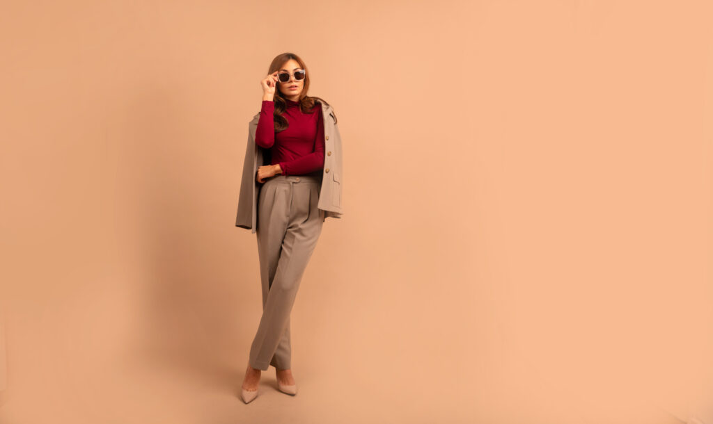 Frau in Anzug mit rotem Pullover vor einem orangefarbenen Hintergrund.