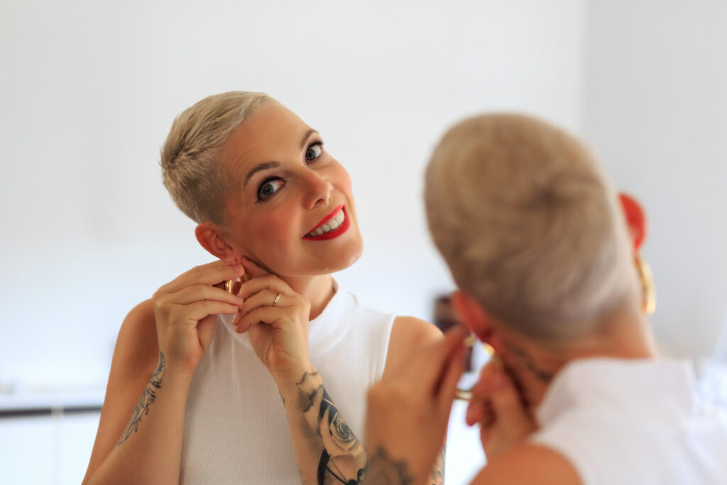 Junge Frau mit Buzz Cut stylt sich mit Ohrringen.