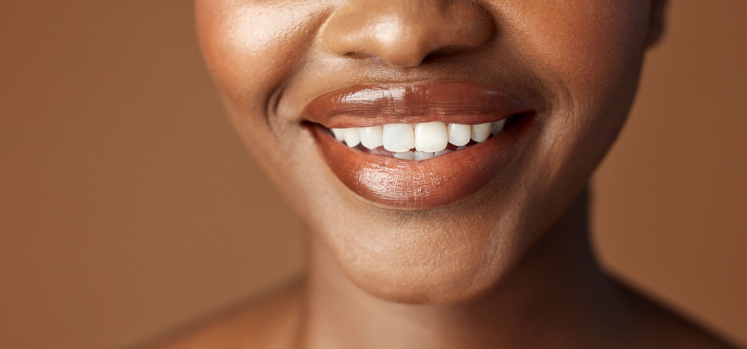 Die untere Hälfte eines weiblichen Gesichts ist zu sehen. Die Lippen sind bräunlich geschminkt und die Person lächelt.