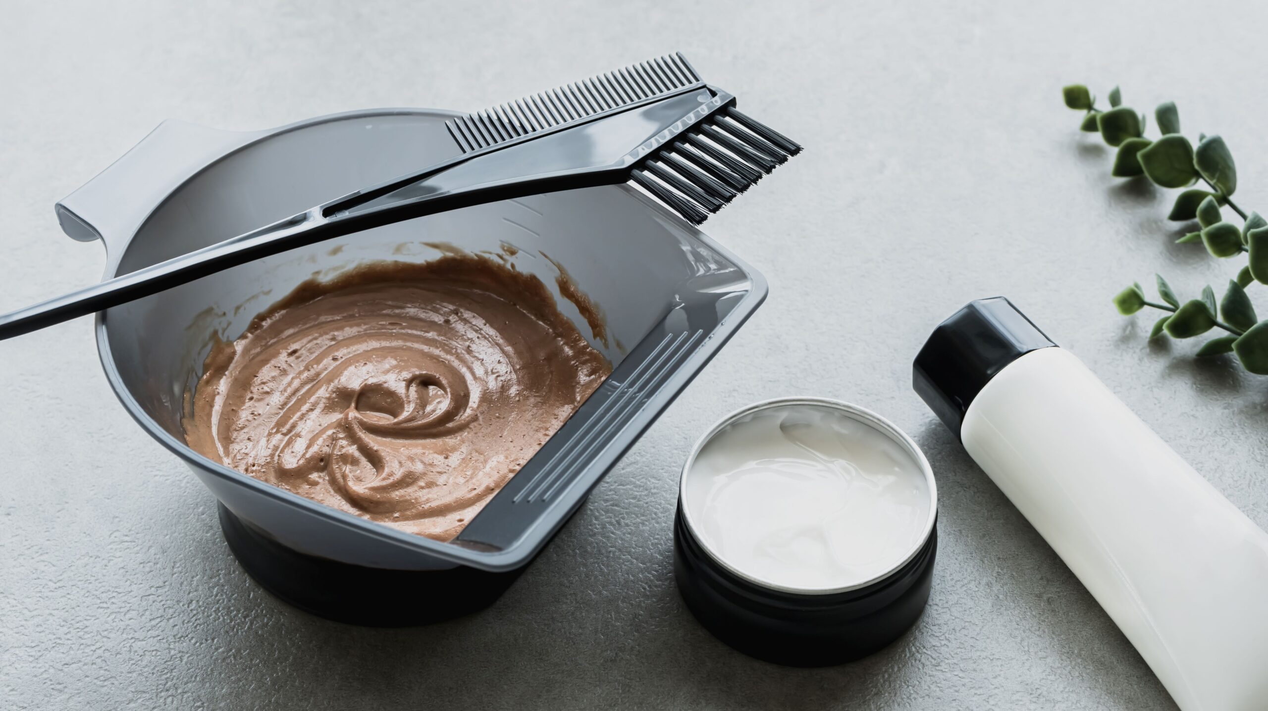 Eine Schäle mit angerührter Haarfarbe steht auf einer grauen Oberfläche. Daneben befinden sich weitere Tools für die Haarfärbung.