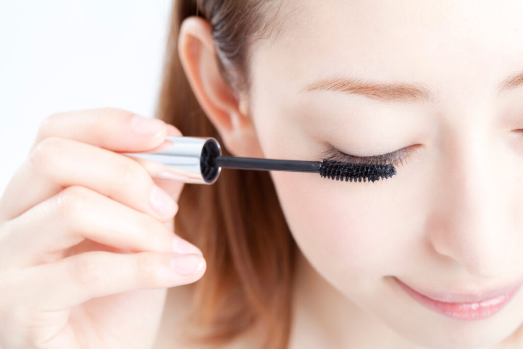 Frau trägt mit einer Bürste Mascara auf die Wimpern auf.