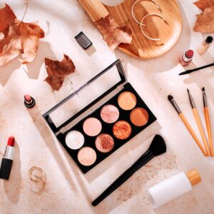 Mehrere Make-Up Produkte liegen auf einem herbstlich gestalteten Untergrund.
