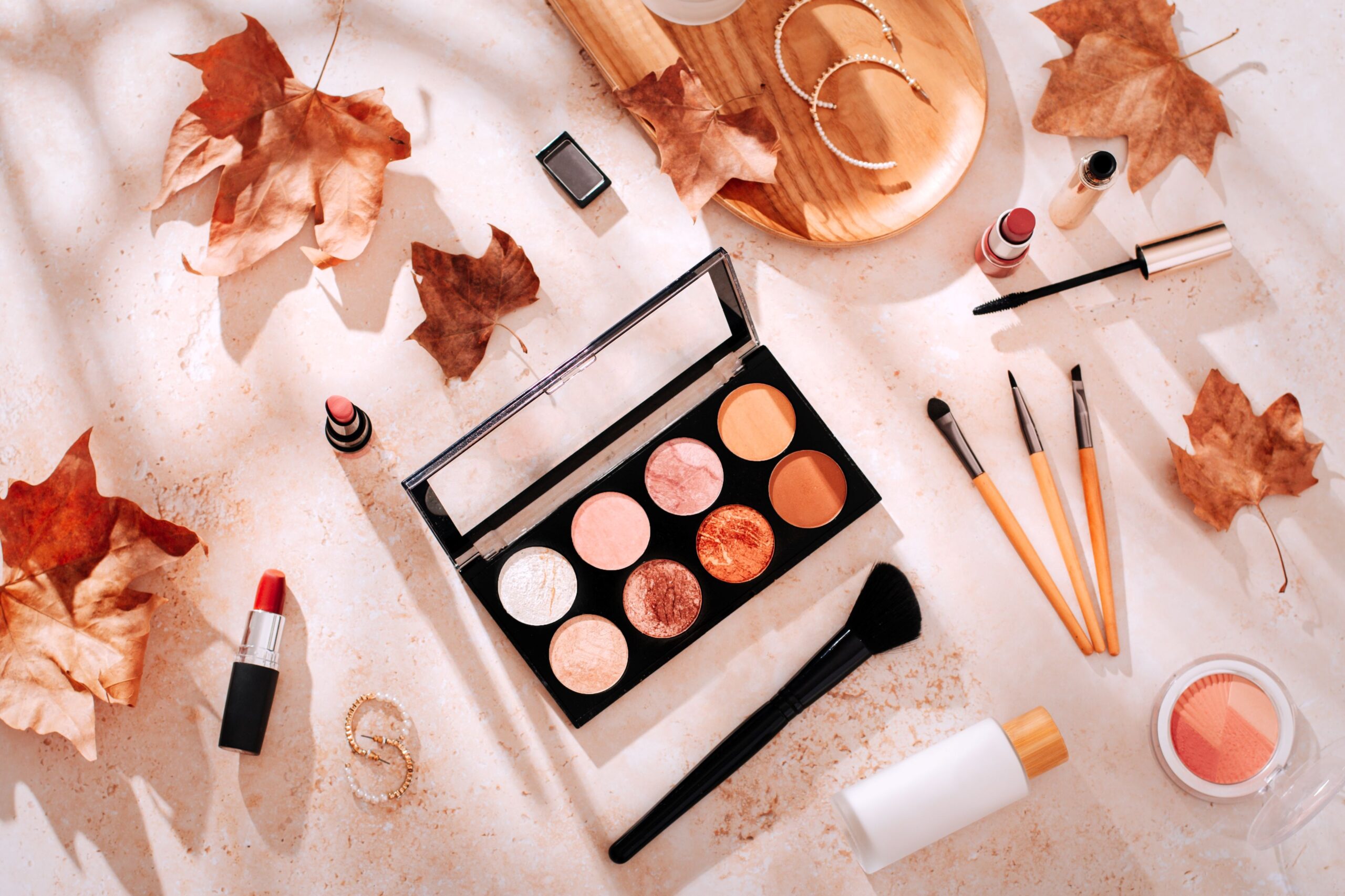 Mehrere Make-Up Produkte liegen auf einem herbstlich gestalteten Untergrund.