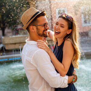 Date-Night-Ideen: Tipps für schöne Abende zu zweit Ein Paar steht vor einem Springbrunnen, hält sich in den Armen und lacht.