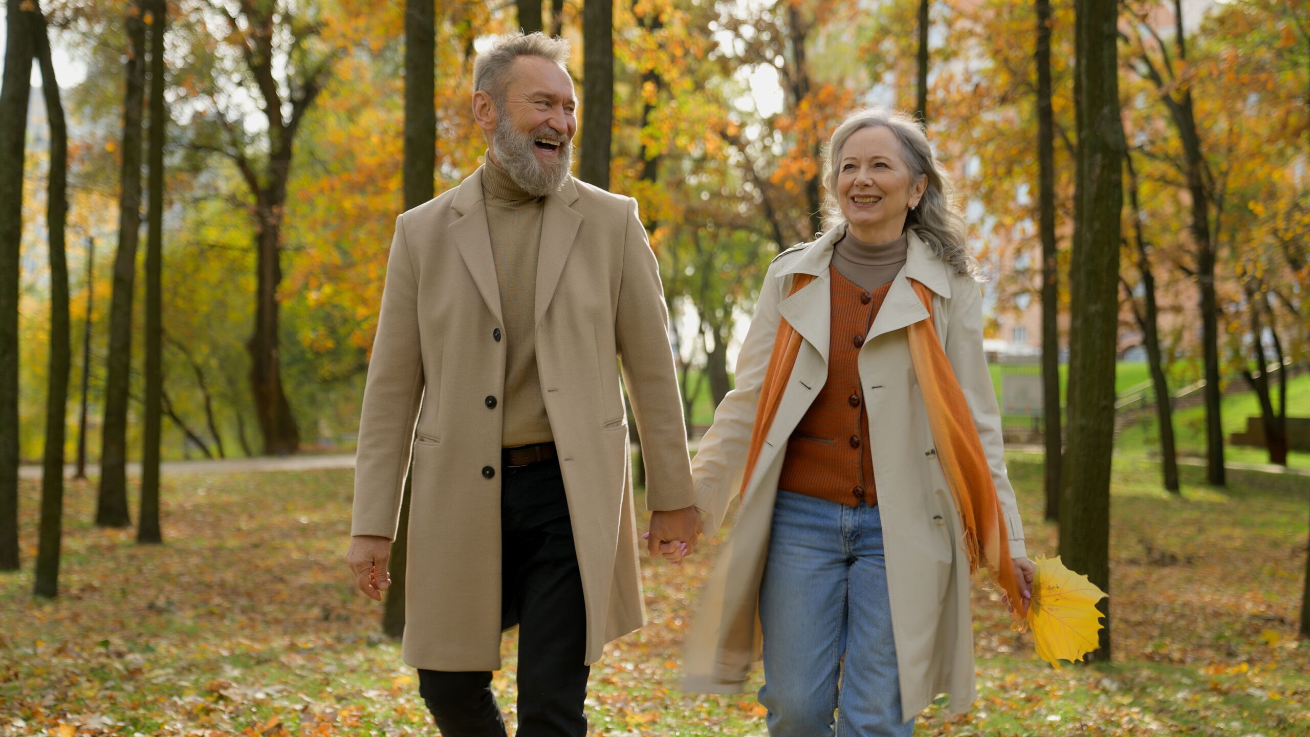 Ein älteres Paar geht im Herbst durch einen Wald. Die Frau hält ein buntes Blatt in der Hand.